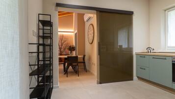Una cocina moderna con puerta corrediza, un comedor con mesa y sillas, y una estantería metálica negra.