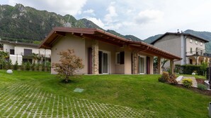 A house with a stone facade, a wooden roof, and a paved lawn with a small tree. - Villa by Lake Idro with Mountain Views (Idro (bs))