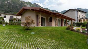 A house with a stone facade, a wooden roof, and a paved lawn with a small tree.