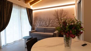 A modern living room with a sofa, a dining table, and a vase of flowers. - Villa by Lake Idro with Mountain Views (Idro (bs))