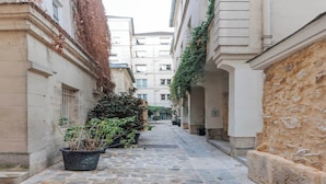 A narrow cobblestone alley flanked by buildings with stone walls and potted plants. - Comfortable Apartment - 1BR/2P - Arts et Métiers (Paris)
