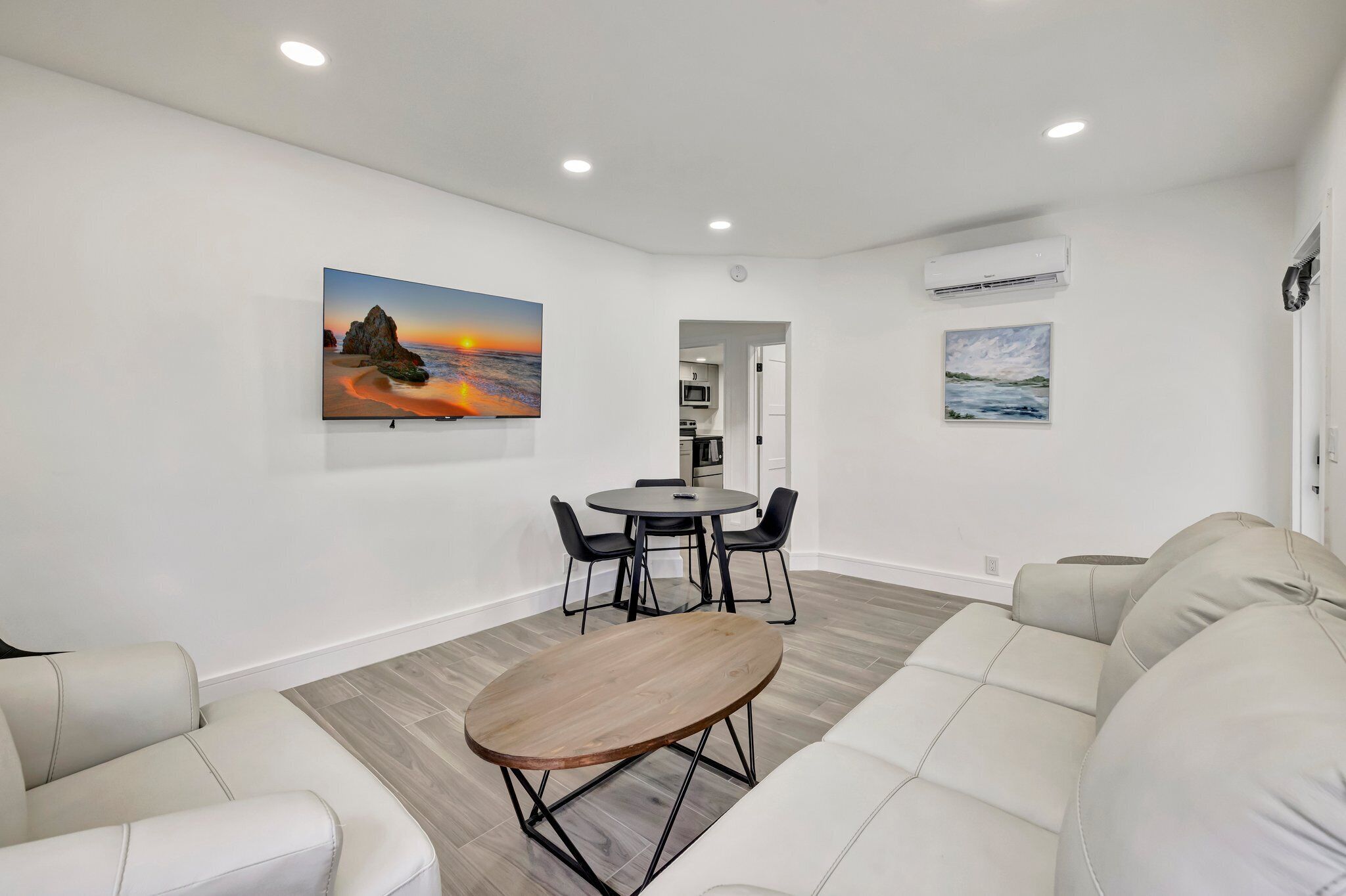 A modern living room with a sofa, a wooden coffee table, a dining table with chairs, and artwork on the walls.