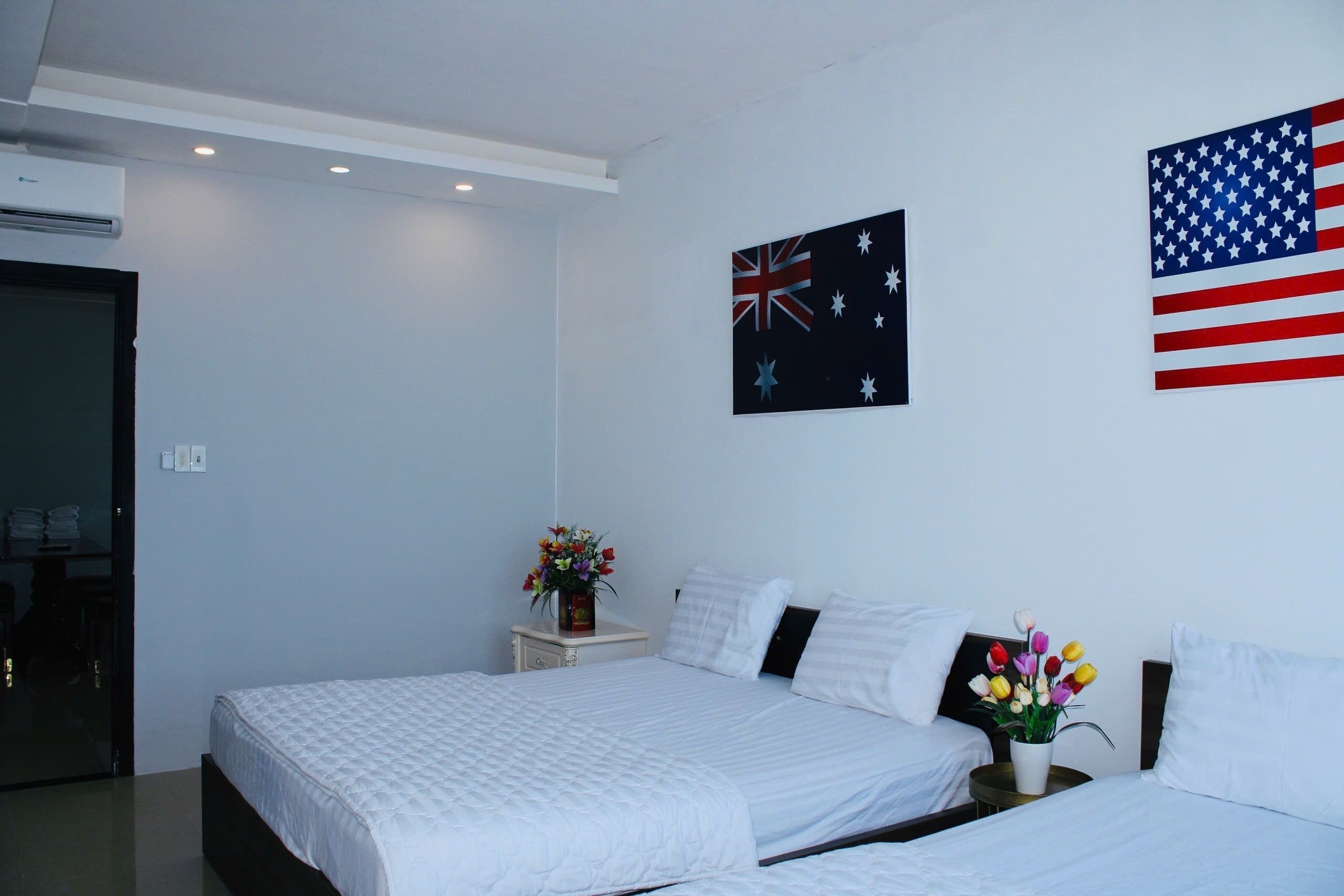 A hotel room with a bed, a nightstand with a vase of flowers, and two flags on the wall.