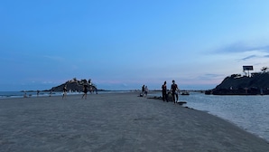 Ein Strand mit Menschen, die laufen und stehen, ein klarer Himmel und Felsen in der Ferne.