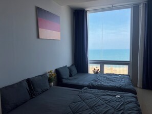 Une chambre d’hôtel avec deux lits, une grande fenêtre donnant sur la plage et un tableau accroché au mur.