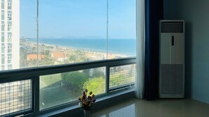 Ein Zimmer mit großem Fenster und Blick auf die Küste, einer weißen Klimaanlage und einem Blumenvasenbrett.