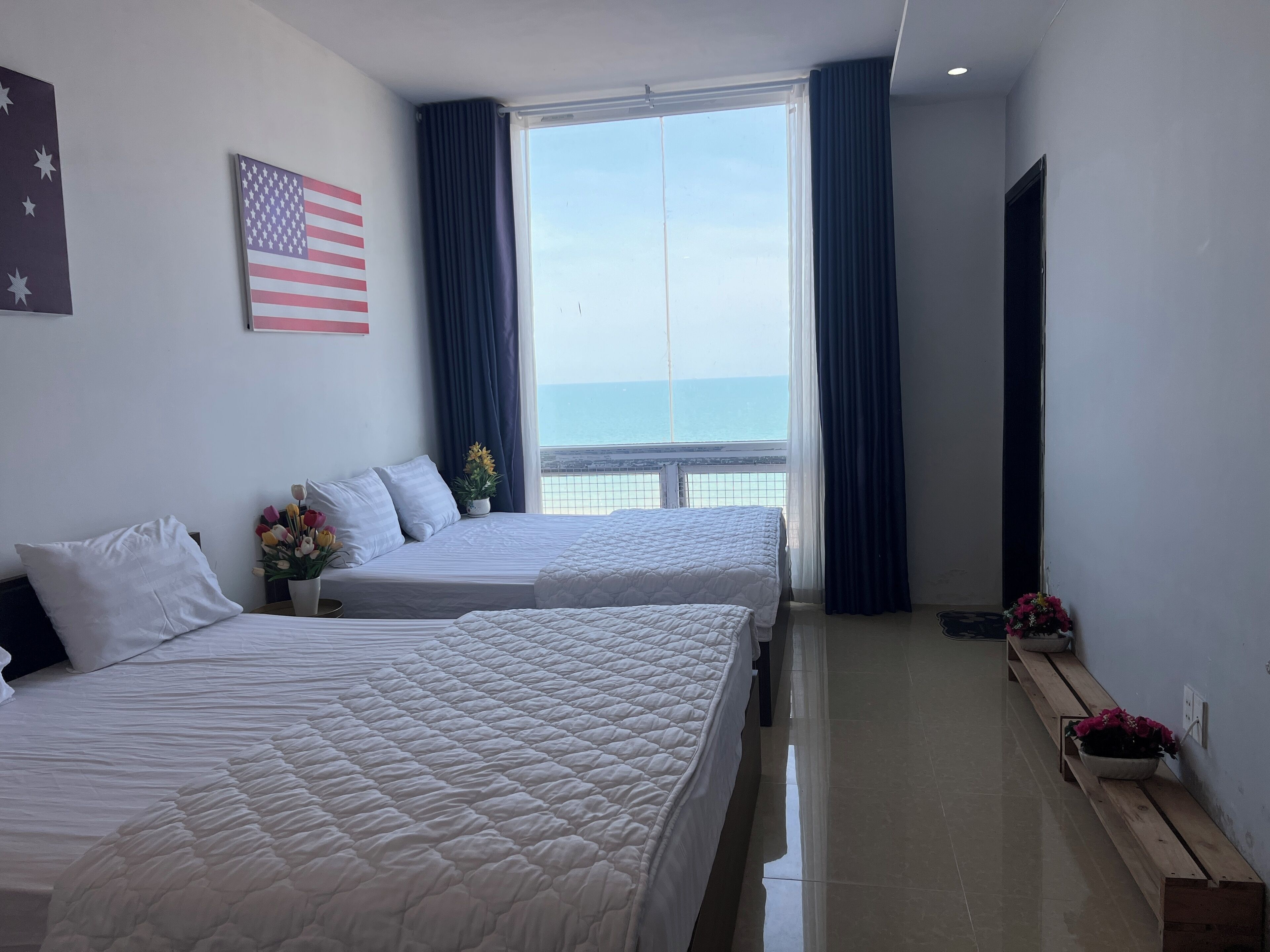 A hotel room with two beds, a large window with a view of the sea, and a small balcony.