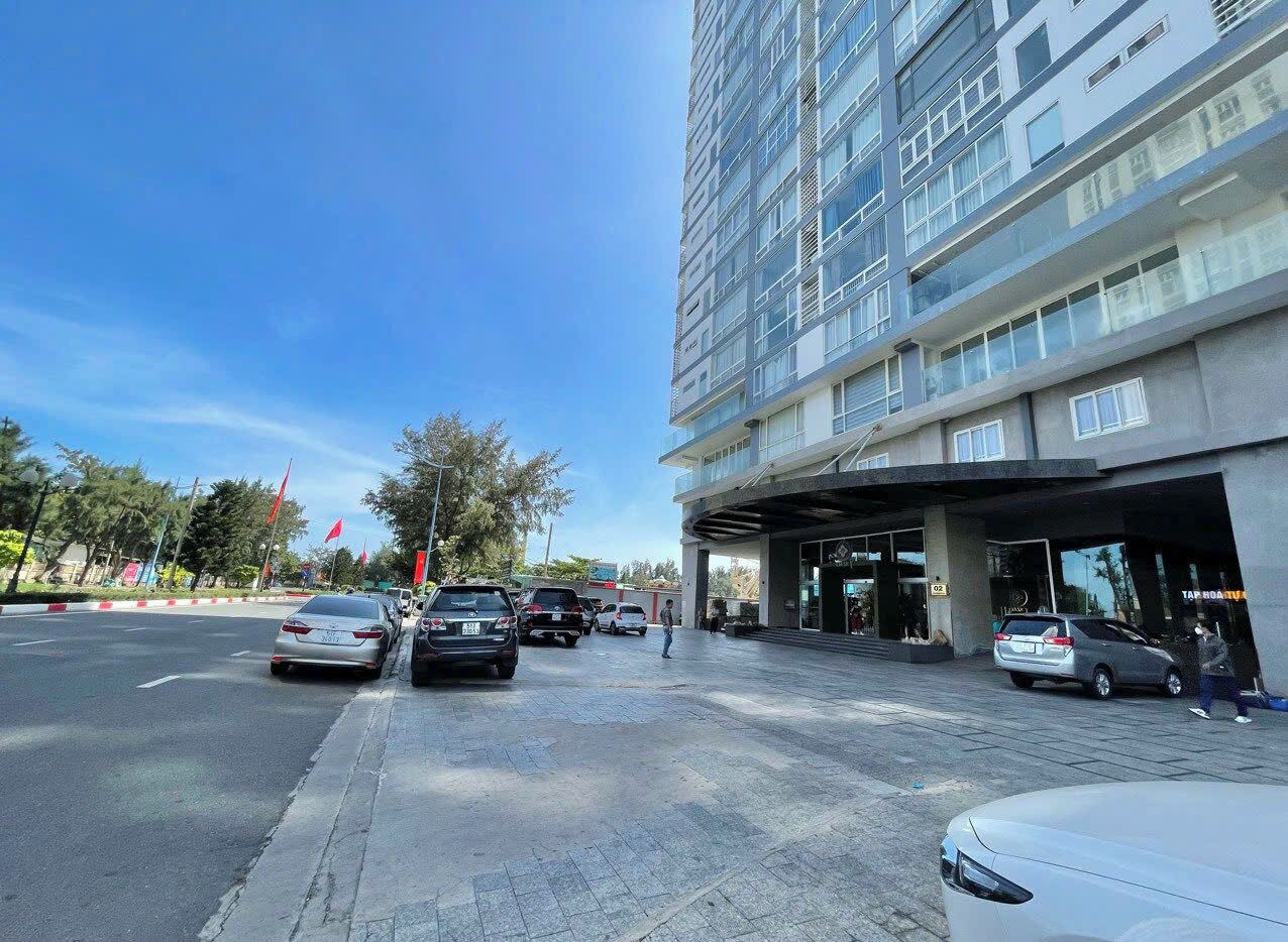 A modern building with a covered entrance, multiple cars parked in front, and a clear blue sky.