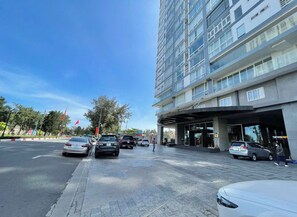 A modern building with a covered entrance, multiple cars parked in front, and a clear blue sky.