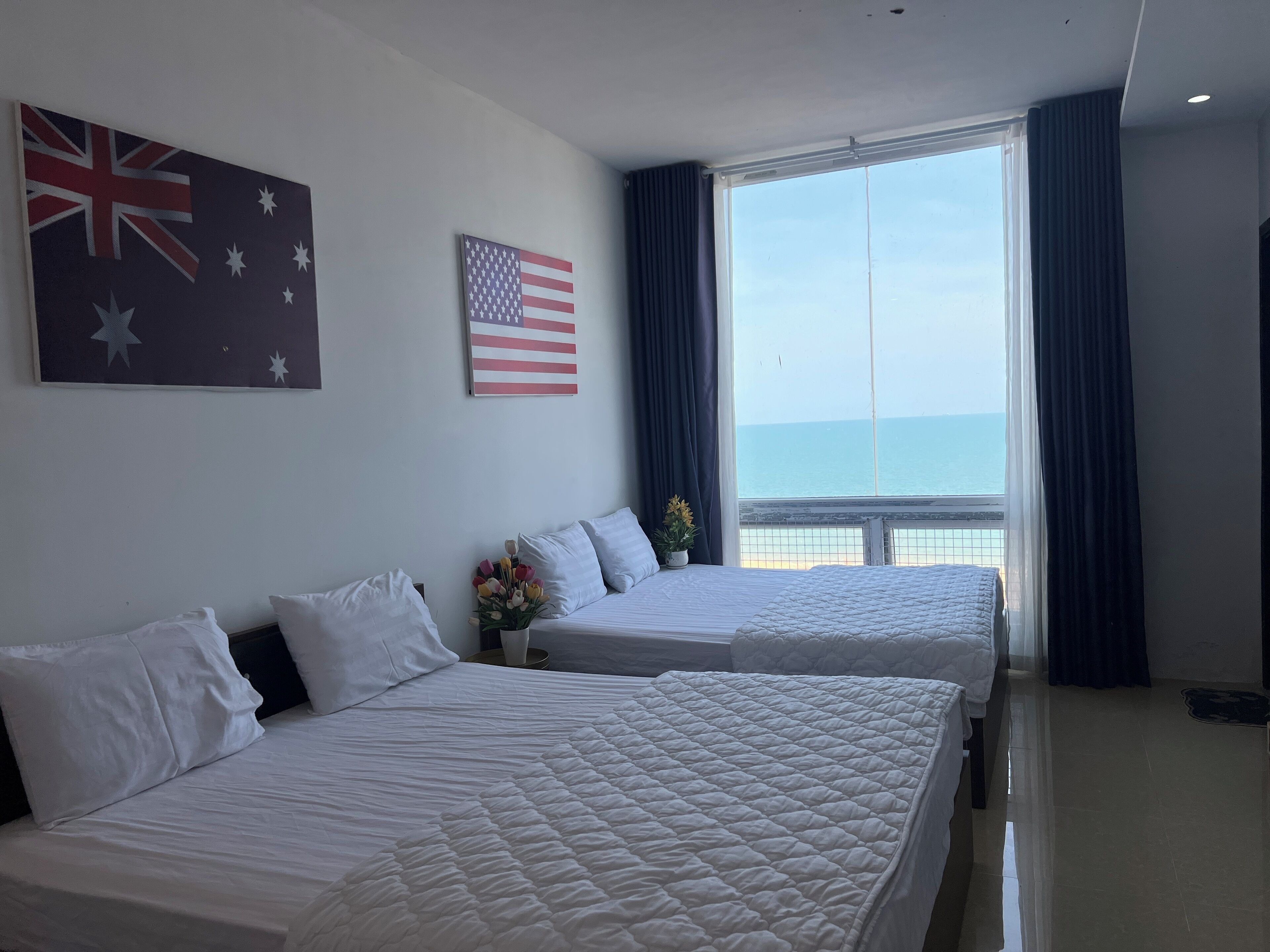 A hotel room with two beds, a large window with a view of the sea, and two flags on the wall.