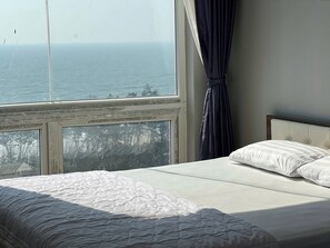 A bedroom with a bed, a view of the sea, and a window with curtains.