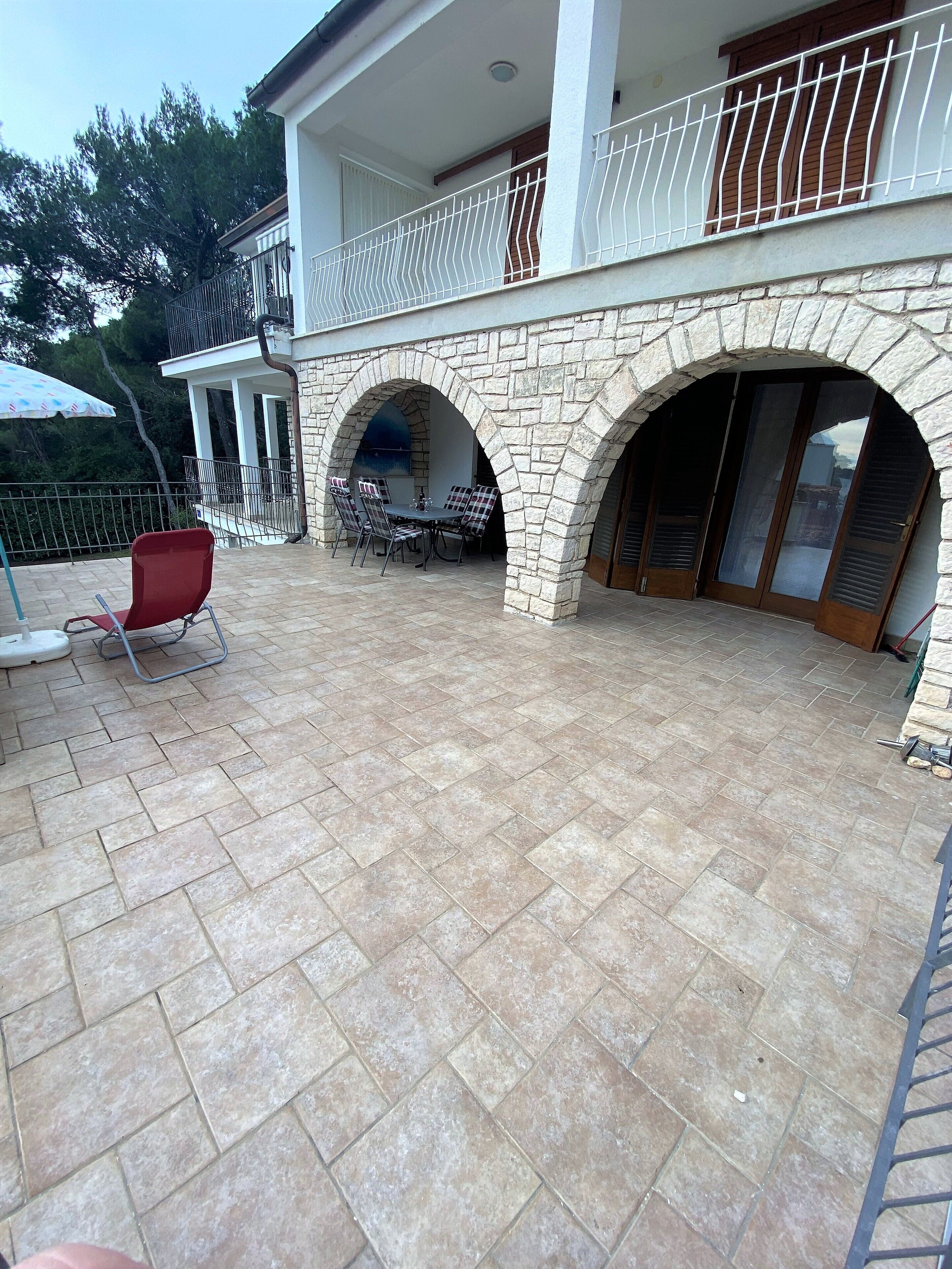Un patio techado al aire libre con arcos de piedra, una mesa de comedor con sillas y una silla roja.