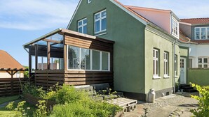 Une maison à deux étages avec une véranda en bois, un petit jardin et un escalier apparent menant à l’étage supérieur.