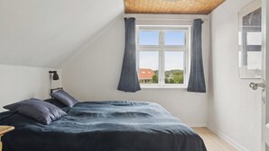 Une chambre à coucher avec un lit, une fenêtre avec des rideaux, un plafond en bois et une porte.