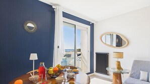 A room with a dining table set with fruits and drinks, a sofa, and a view of the city through a large window.