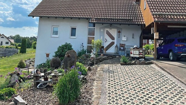 Une maison à deux étages, avec un toit en tuiles, un garage et une allée pavée avec des motifs.
