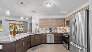 A modern kitchen with a stainless steel refrigerator, dark wooden cabinets, a built-in oven, and a dishwasher. - Ohia Lehua Hale-Hot Tub-Fireplace-Fire Table-3-Bed, 2-Bath Newly Renovated Home (Volcano)
