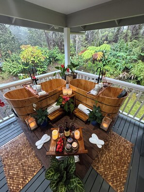 Un espacio de estar al aire libre cubierto, con mobiliario de madera y una mesa lista para comer, con vistas a un jardín exuberante.