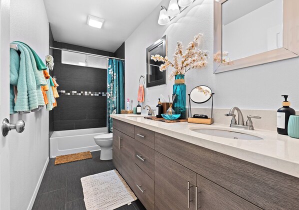 A modern bathroom with a bathtub, toilet, and vanity with a mirror and sink.