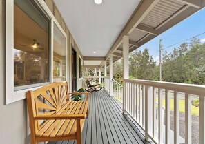 A covered porch with a wooden bench and a rocking chair, white railings, and a view of trees.