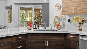 A modern kitchen with a large island, dark wood cabinets, a stainless steel sink, and pendant lighting. - Ohia Lehua Hale-Hot Tub-Fireplace-Fire Table-3-Bed, 2-Bath Newly Renovated Home (Volcano)