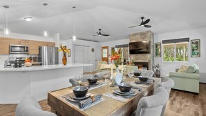 A modern kitchen with a central island, a dining area with a wooden table, grey upholstered chairs, and a green sofa. - Ohia Lehua Hale-Hot Tub-Fireplace-Fire Table-3-Bed, 2-Bath Newly Renovated Home (Volcano)