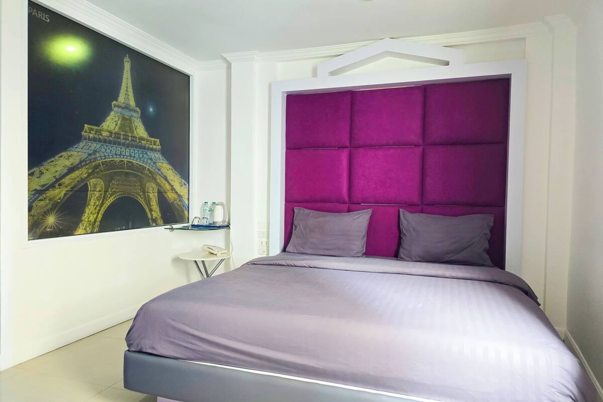 A modern bedroom with a bed, a headboard, a nightstand, and a wall-mounted artwork of the Eiffel Tower.