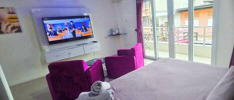 A hotel room with a bed, a TV, a seating area with chairs, and a view of the outside.