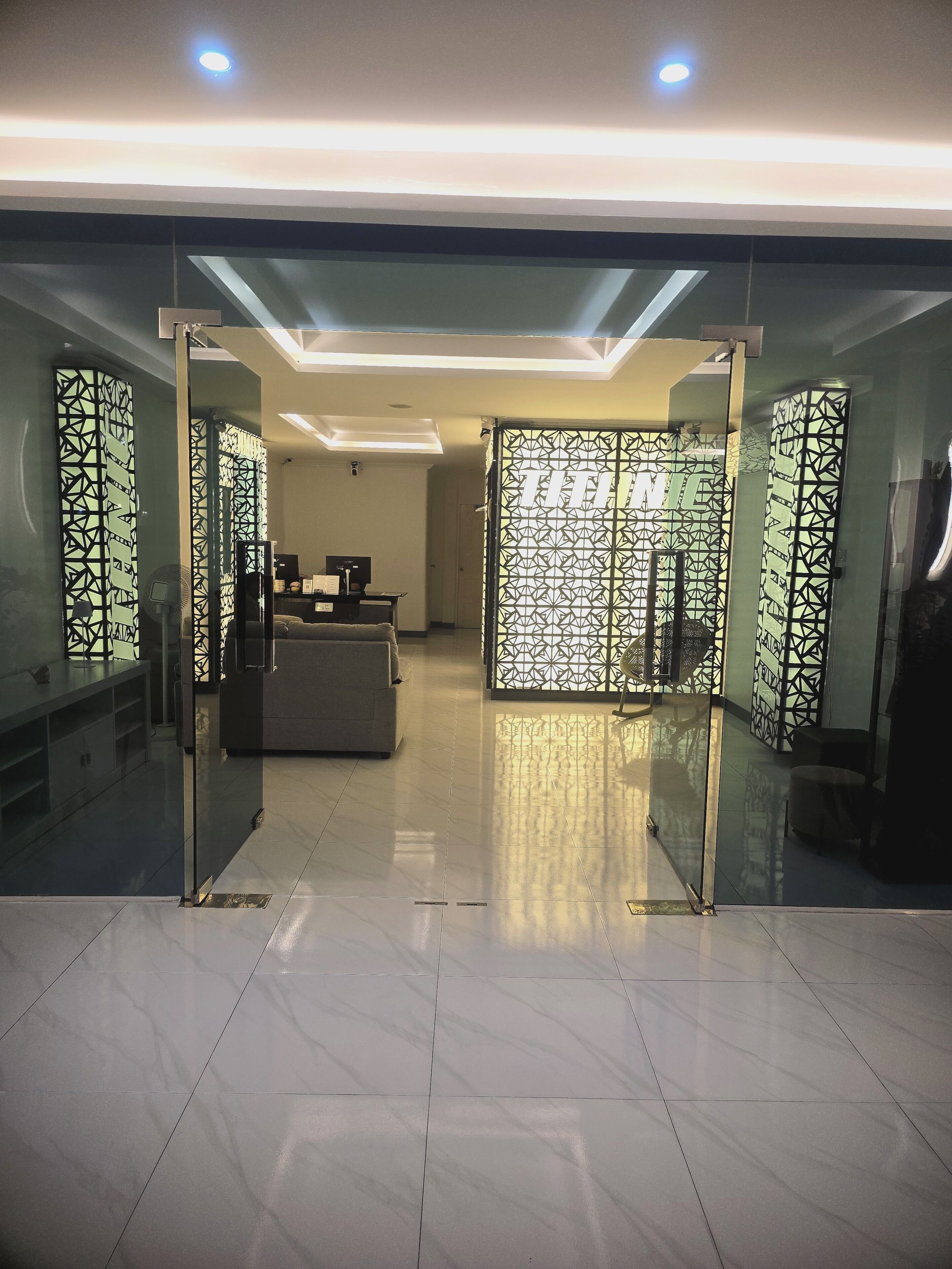 A modern hotel lobby with a reception desk, seating area, and decorative glass partitions.