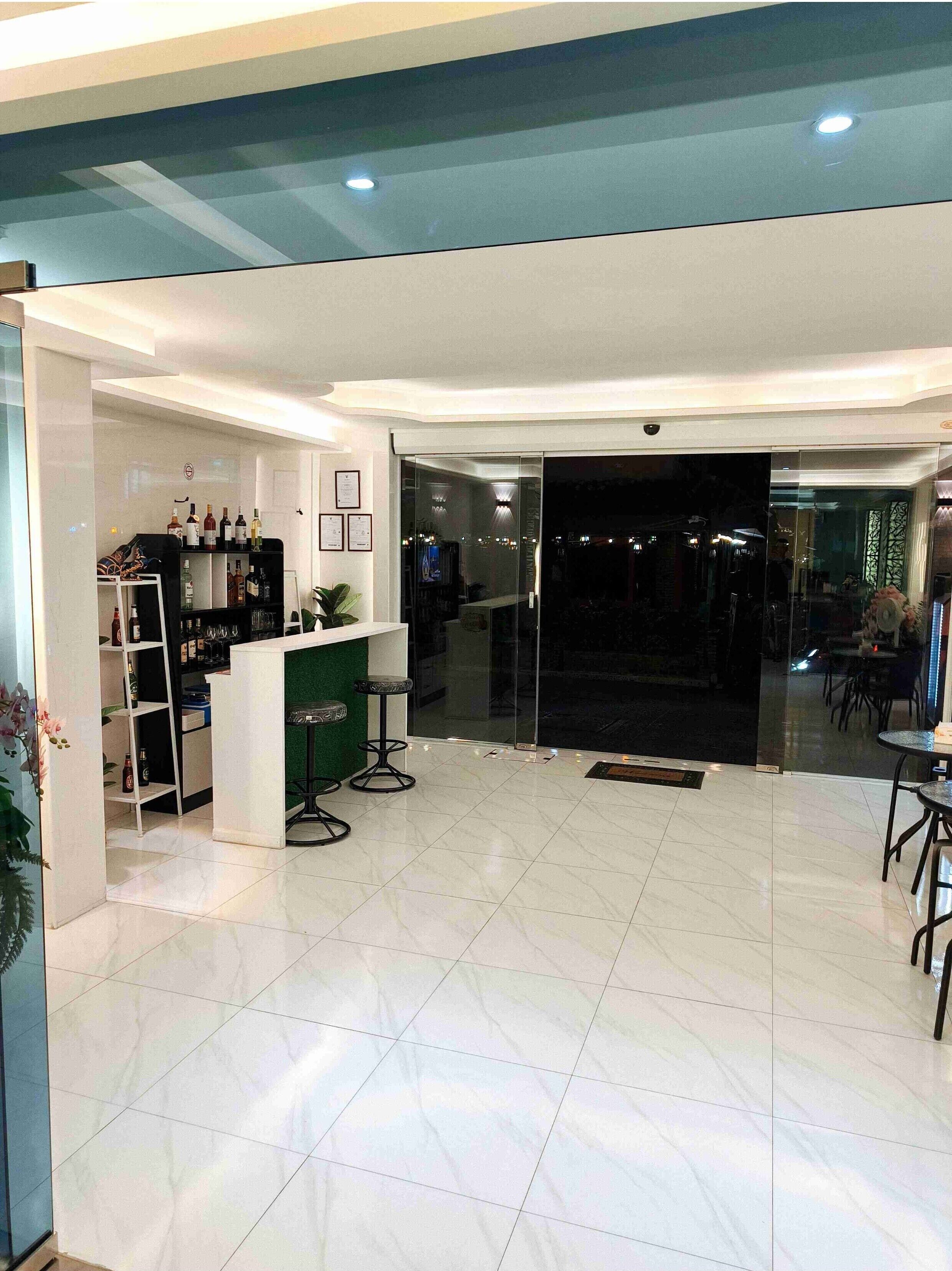 A modern bar area with a white countertop, shelves with bottles, and stools.