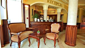 Un área de recepción con dos sillas de madera, una mesa pequeña con una planta y un mostrador de recepción con un letrero que dice "RECEPCIA".