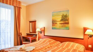Habitación de hotel con una cama grande, un escritorio, una silla, un cuadro en la pared y una ventana con cortinas.