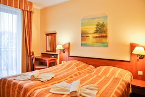 Quarto de hotel com uma cama grande, uma escrivaninha, uma cadeira, um quadro na parede e uma janela com cortinas.