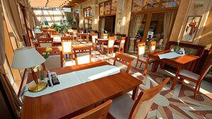 Un restaurante con mesas y sillas de madera, piso de baldosas y amplias ventanas.