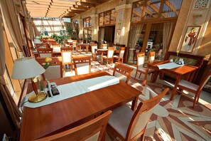 Um restaurante com mesas e cadeiras de madeira, piso de azulejos e grandes janelas.