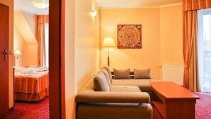 Habitación de hotel con sofá, cama con alfombra roja, mesa de madera y lámpara de pared.