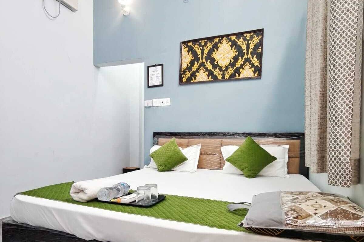 A neatly made bed with green and white pillows, a decorative wall piece, and a bedside table with a tray.