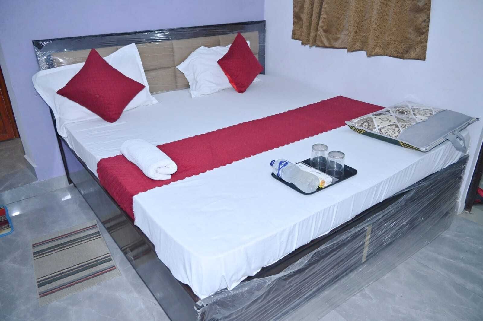 A neatly made bed with white and red bedding, a rolled towel, and a tray with a bottle and glasses.