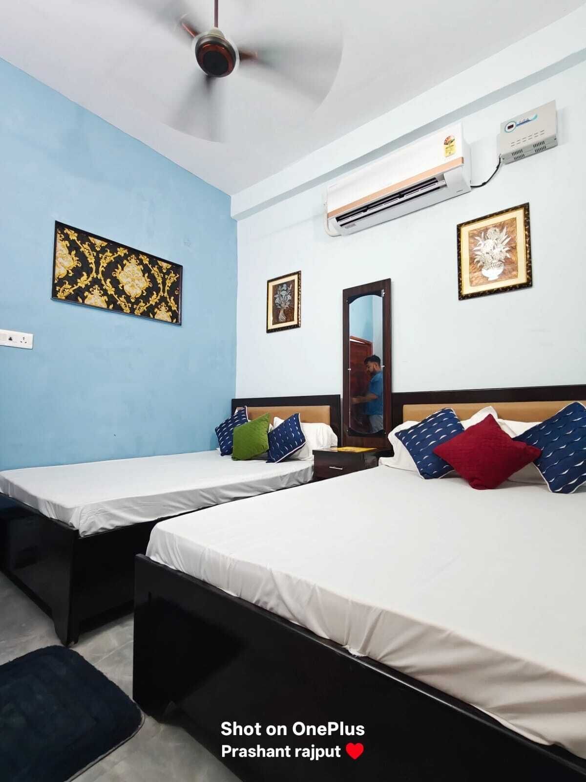 Ein Hotelzimmer mit zwei Einzelbetten, einem Deckenventilator, einer Klimaanlage und gerahmten Kunstwerken an den Wänden.