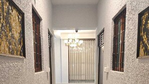 A hallway with textured walls, a chandelier, and a view into a room with a bathtub. - The Nest Ayodhya (Faizabad)