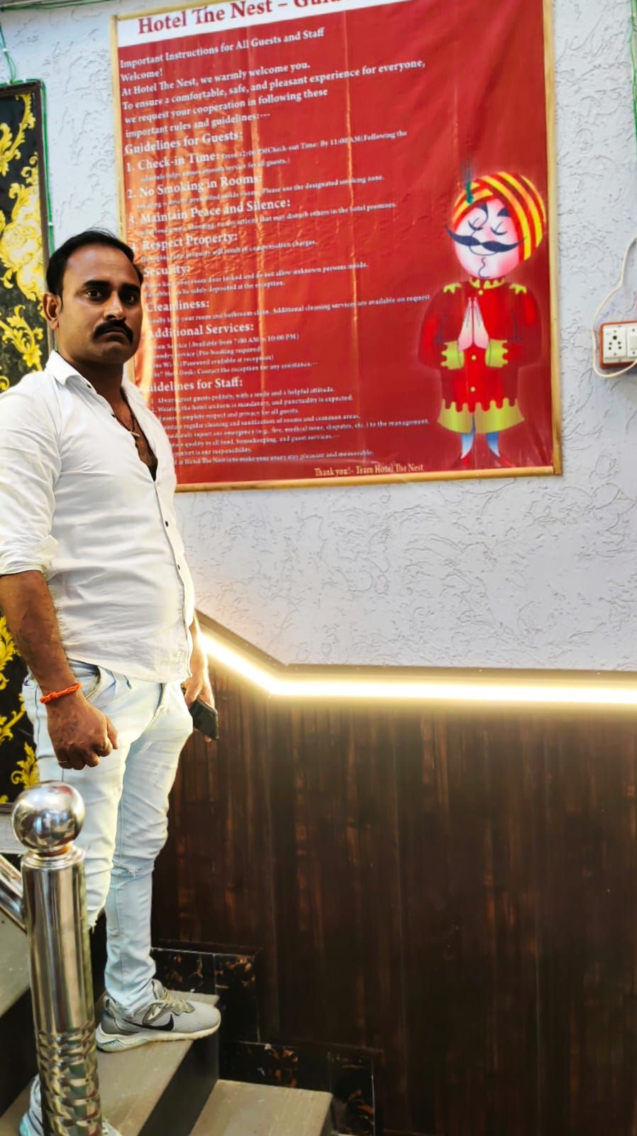 A man standing next to a hotel sign with guidelines for guests and staff.