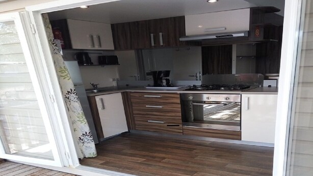 A modern kitchen with wooden cabinets, a gas stove, and a built-in oven. - SABLES DU MIDI LOCATION CLIM 3CH 2SDB CAMPING VOS VACANCES (Valras-Plage)