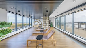Un espacio lounge moderno con bancos y mesas de madera, amplias ventanas que ofrecen vistas de la ciudad y un techo con un diseño geométrico único.