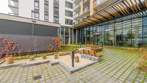 Un espacio moderno al aire libre con un sendero pavimentado, bancos de madera y un frente de edificio de vidrio.