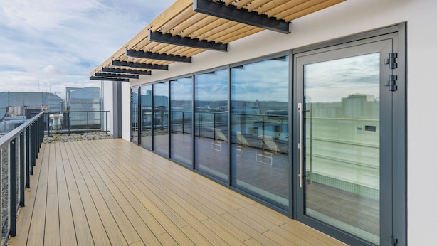 Una terraza moderna en la azotea con cubierta de madera, puertas de cristal grandes y una pérgola de madera.