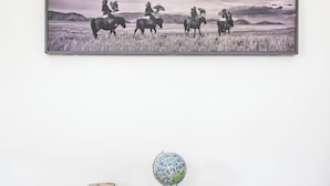 Fotografía en blanco y negro enmarco, mostrando jinetes a caballo en un campo, una pequeña mesa de madera con un globo terráqueo y un tazón, y un suelo de madera.