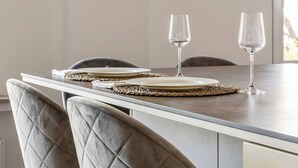 Una mesa de comedor con copas de vino y platos, sillas acolchadas y vistas al exterior.