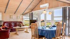 Een gezellige kamer met een houten plafond, een rode leren bank, een eettafel met stoelen en grote ramen met uitzicht op de omgeving.