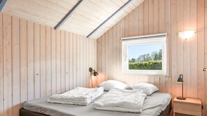 Een slaapkamer met een bed, een raam met uitzicht, een bedlamp en een houten plafond.