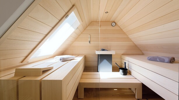 Una habitación pequeña de madera con techo inclinado, un banco, una mesita y una cama.